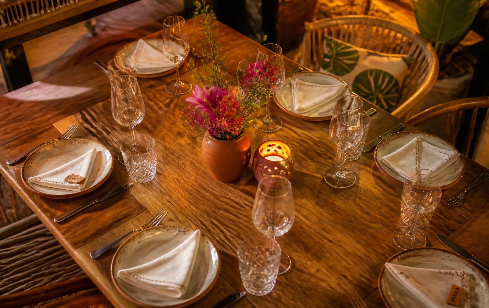 Mesa posta com pratos de cerâmica, copos e flores no Panelinha Carioca